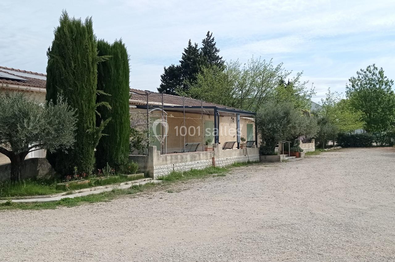 Allée gravillonnée bordée d'arbres et de buissons, longeant une maison avec terrasse et panneaux solaires.