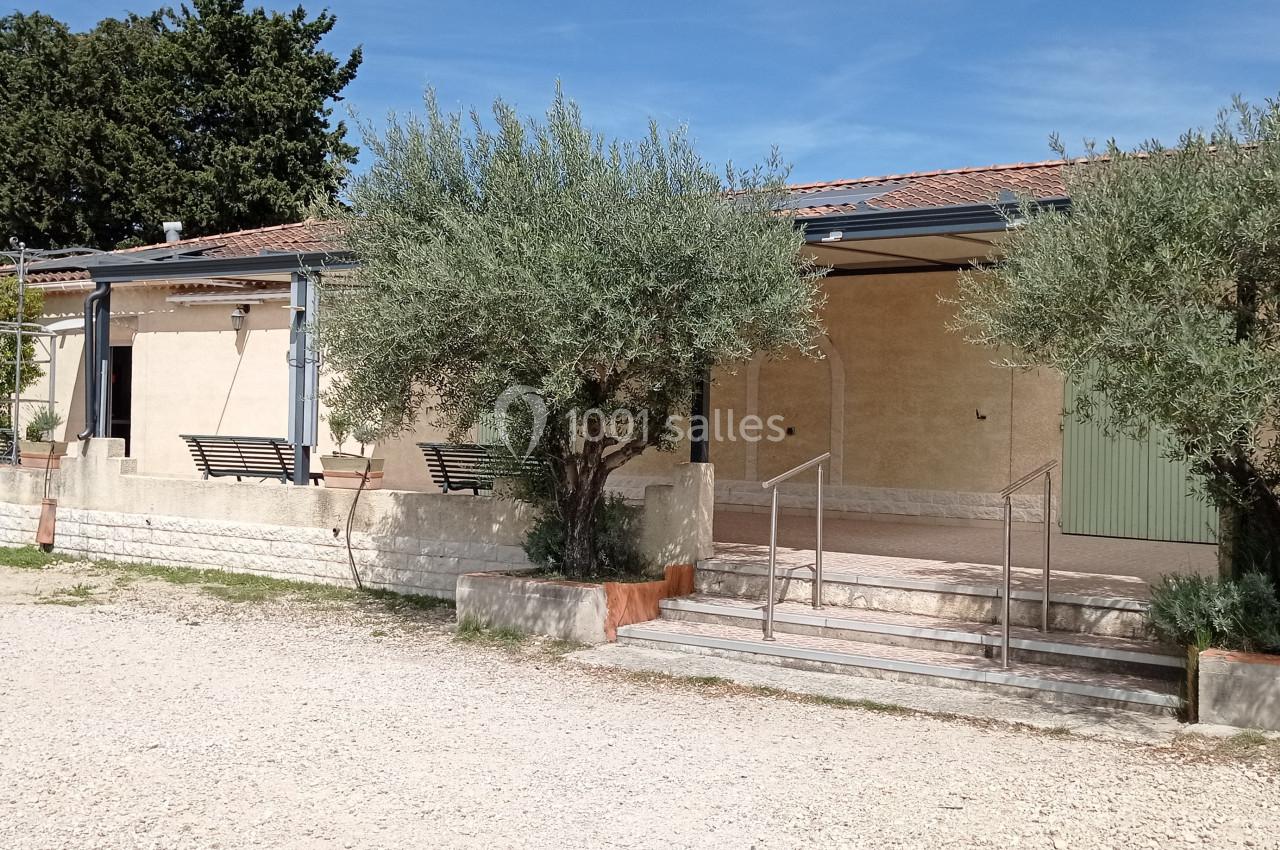 Façade d'un bâtiment avec terrasse, encadrée par des oliviers, sous un ciel dégagé.
