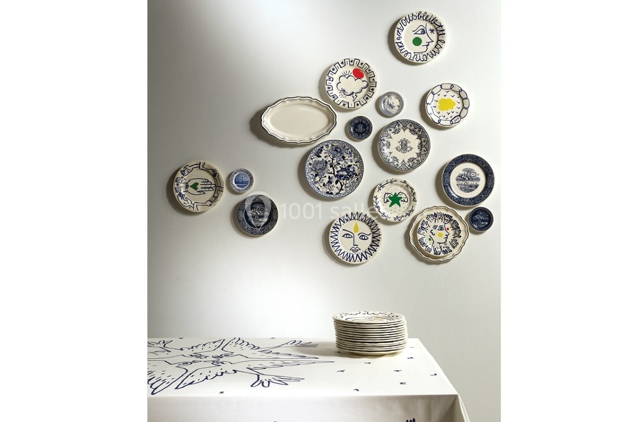 Assortiment de plats et d'assiettes décoratives accrochés au mur au-dessus d'une table dressée avec une nappe blanche.