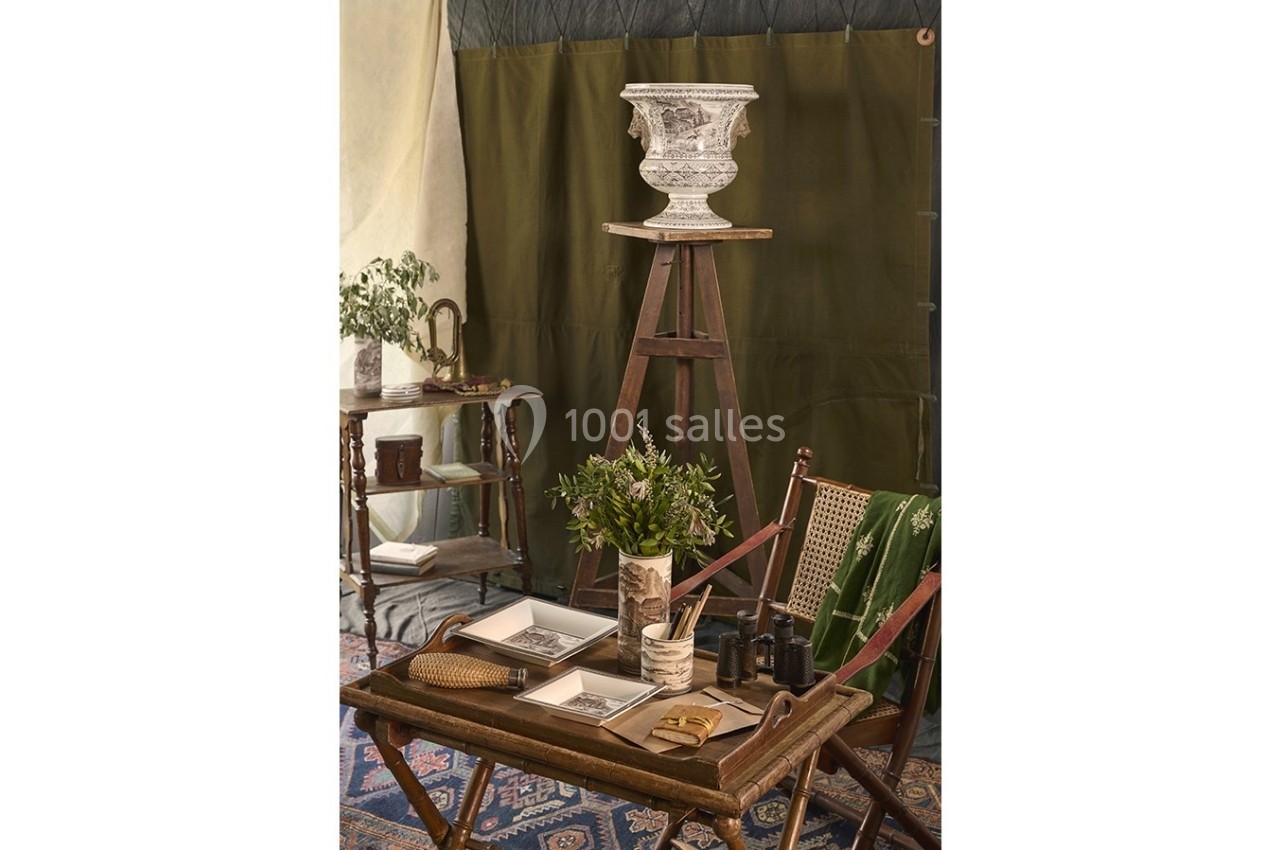 Intérieur décoré de style vintage avec table en bois, objets anciens, plantes et vase sur un chevalet.