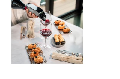 Miniature Aveine #2 Une personne verse du vin rouge dans un verre sur une table dressée avec des pâtisseries et des couverts.