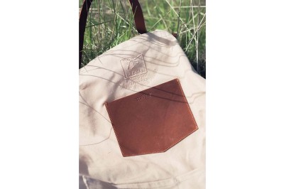 Sac vert en toile imperméable avec poignées noires, posé sur un sol en bois éclairé par la lumière naturelle.