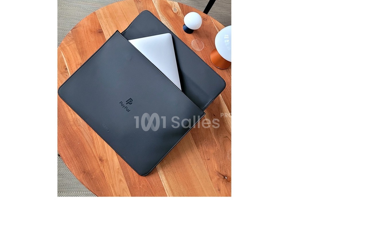 Ordinateur portable argenté partiellement glissé dans une housse noire posée sur une table en bois.