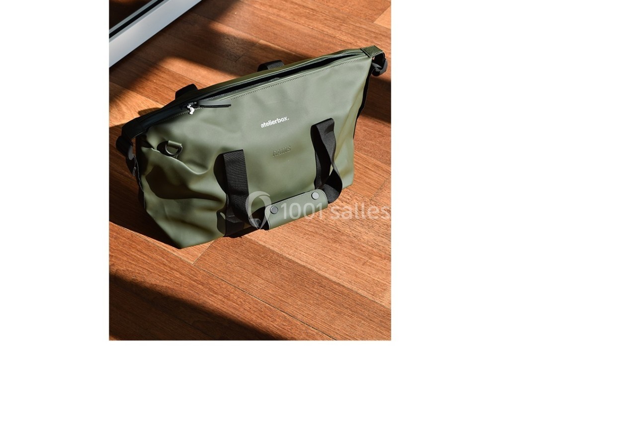 Sac vert en toile imperméable avec poignées noires, posé sur un sol en bois éclairé par la lumière naturelle.