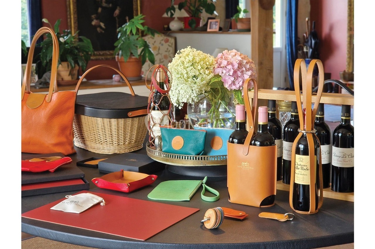 Articles en cuir, paniers, fleurs et bouteilles de vin disposés sur une table dans un intérieur chaleureux.