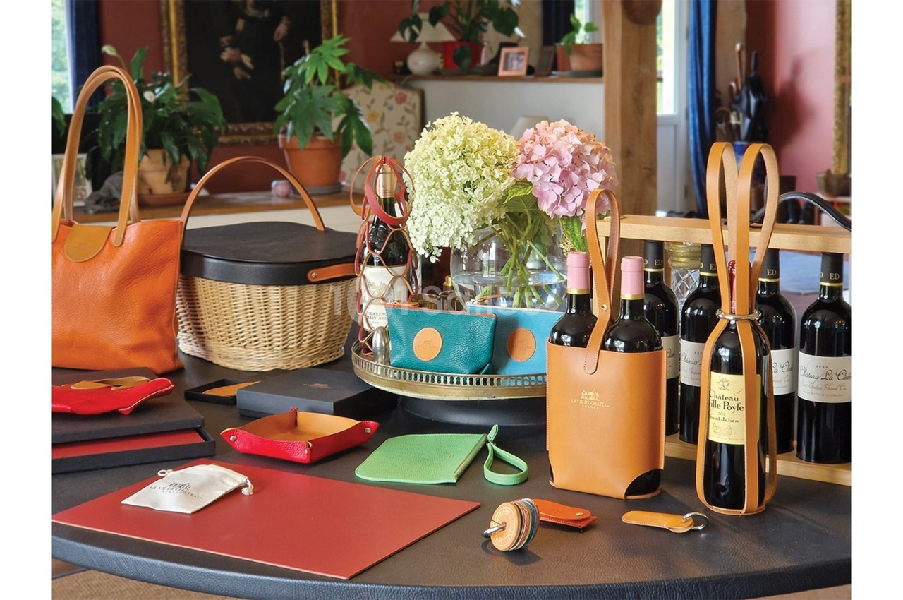 Articles en cuir, paniers, fleurs et bouteilles de vin disposés sur une table dans un intérieur chaleureux.