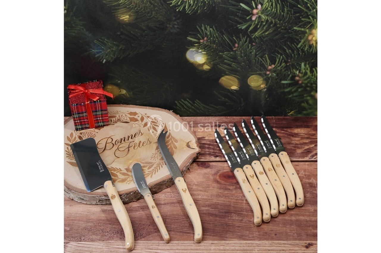 Plateau en bois gravé ’Bonnes Fêtes’ avec couteaux à manche clair, hachette et décorations de Noël en arrière-plan.