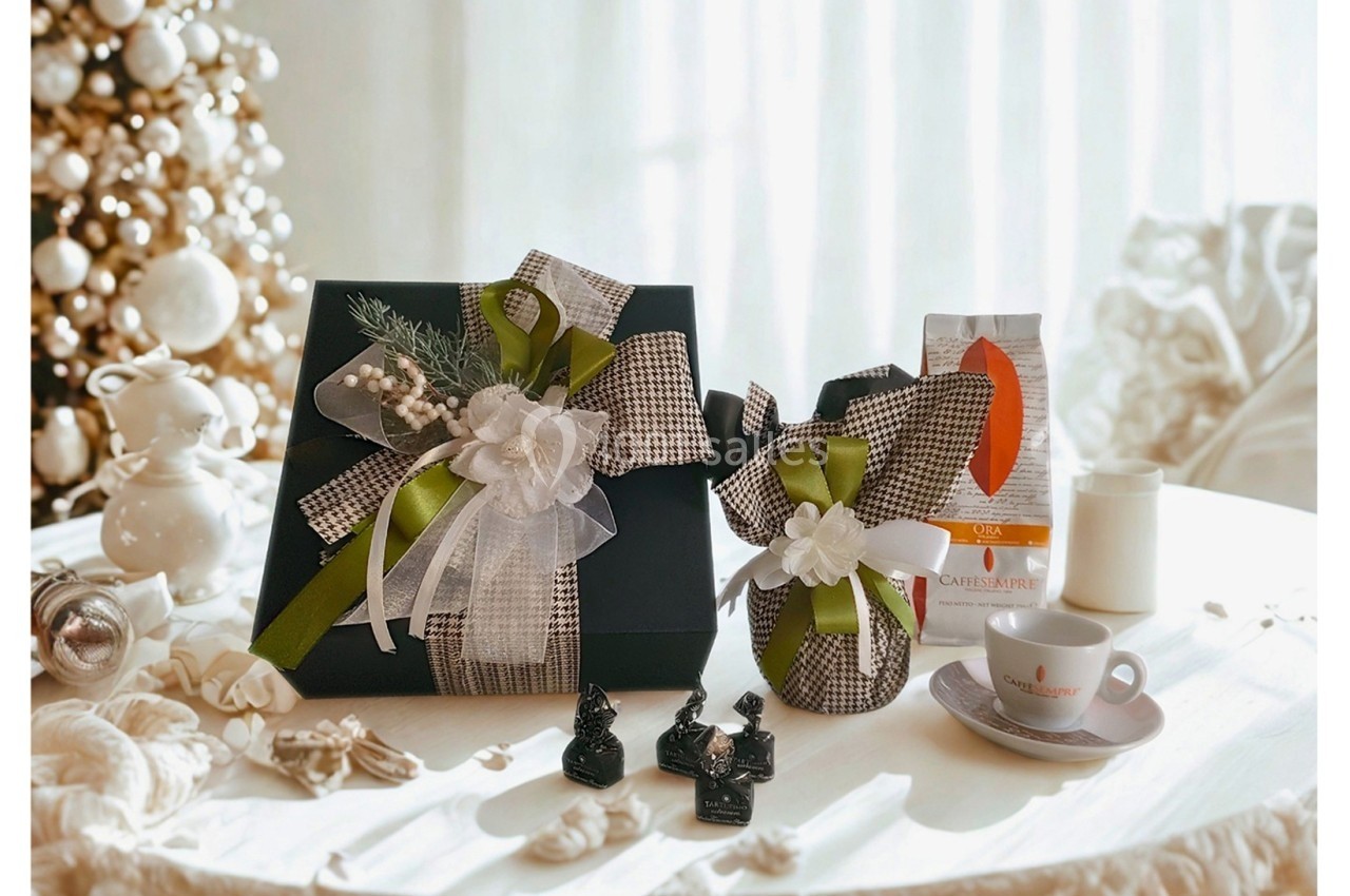 Coffret cadeau élégant avec rubans, sachets décorés, tasse et café sur une table près d'un sapin de Noël.