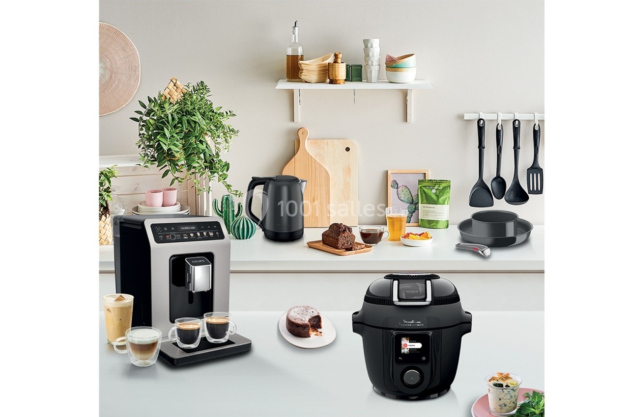Cuisine moderne avec cafetière, autocuiseur, bouilloire, ustensiles suspendus et plan de travail décoré.