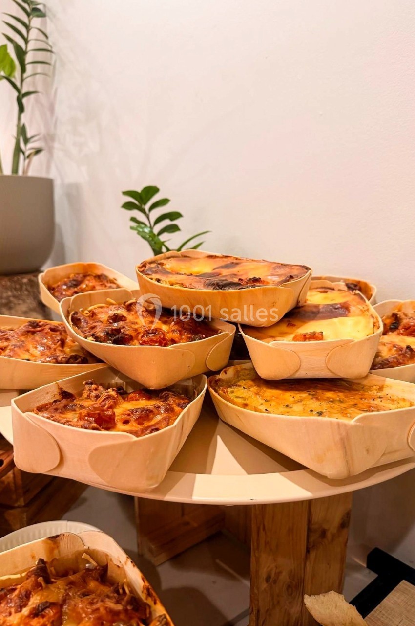 Quiches variées présentées dans des moules en bois sur une table, avec des plantes en arrière-plan.