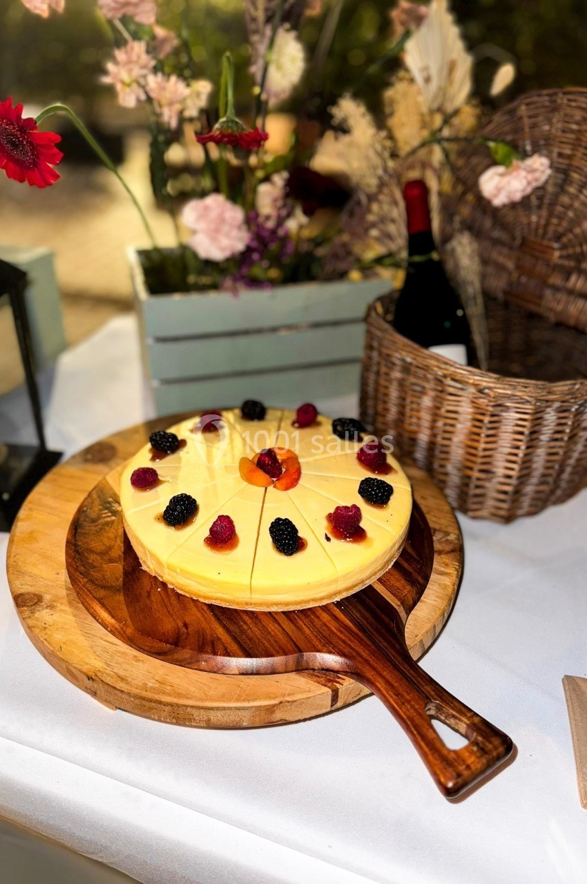 Tarte au citron décorée de fruits rouges et d'orange, posée sur une planche en bois dans un décor champêtre.