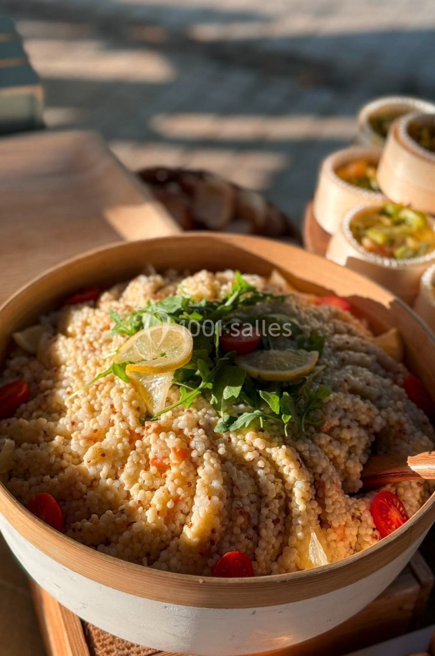 Salade de couscous perlé garnie de roquette, rondelles de citron et tomates cerises, servie dans un bol en bois.