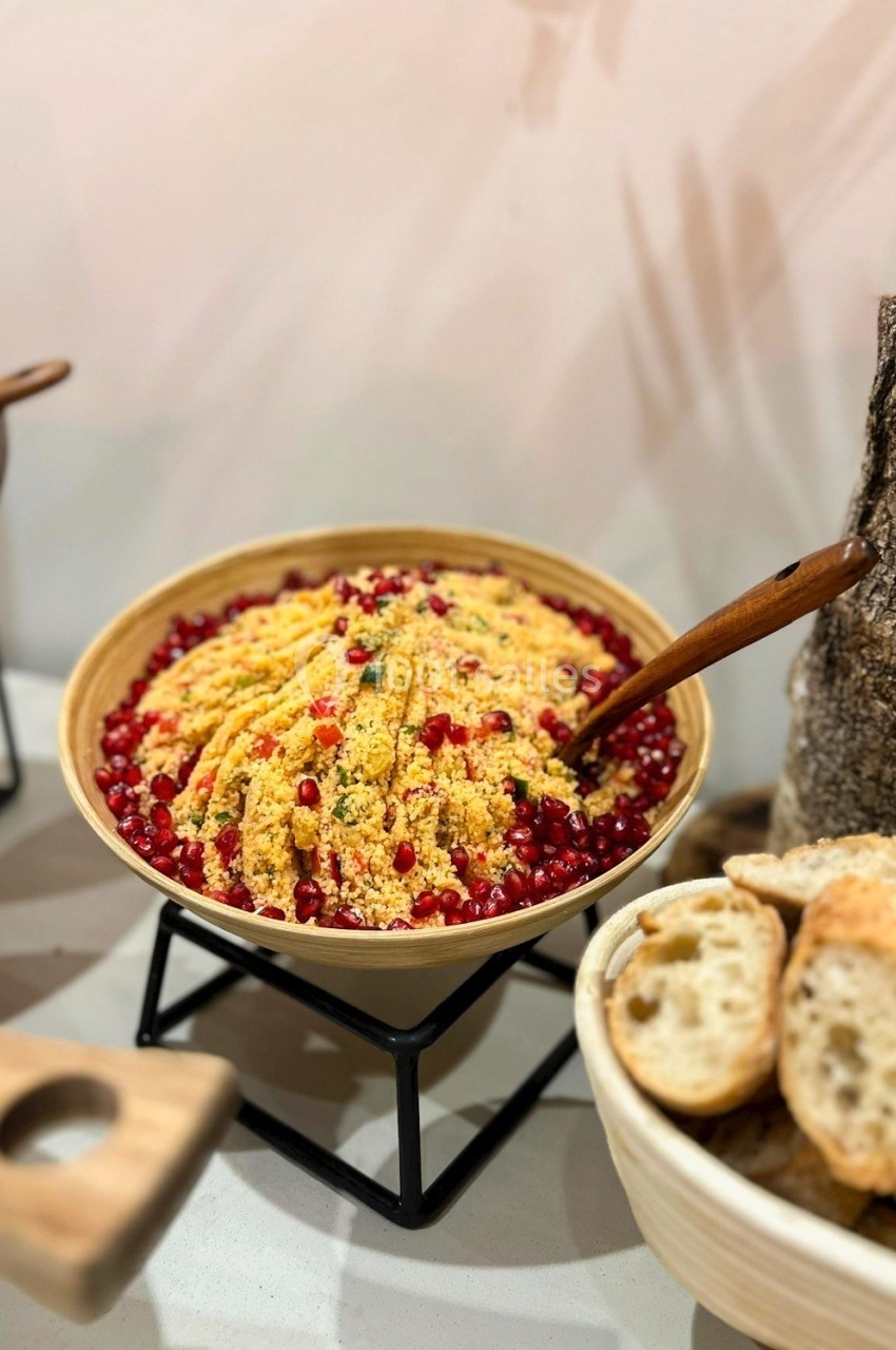 Salade de couscous garnie de graines de grenade dans un bol en bois, accompagnée de tranches de pain.
