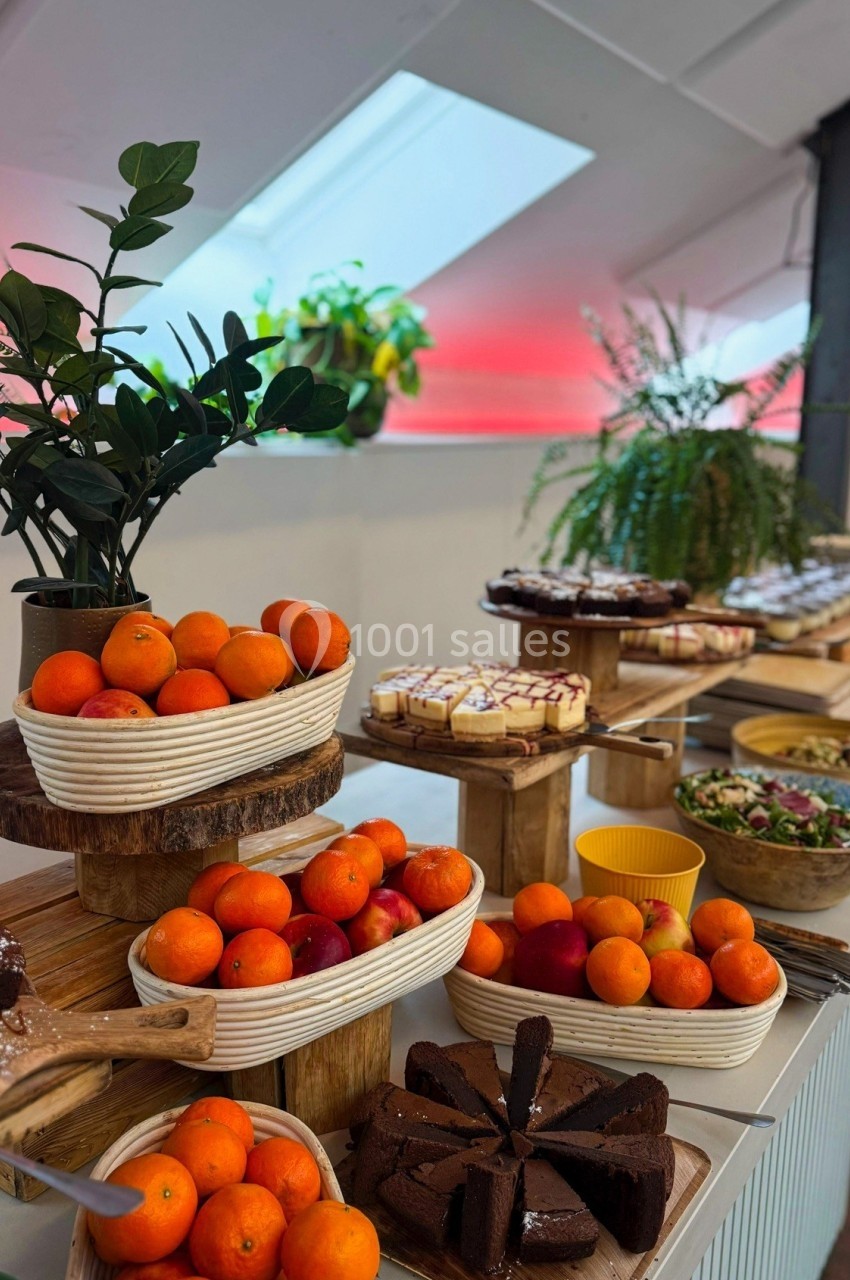 Buffet avec mandarines, gâteaux, salades et plantes décoratives dans un espace lumineux.