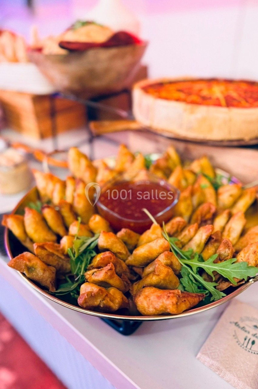Assortiment de samoussas dorés avec sauce rouge au centre, décoré de roquette, présenté sur une table de buffet.