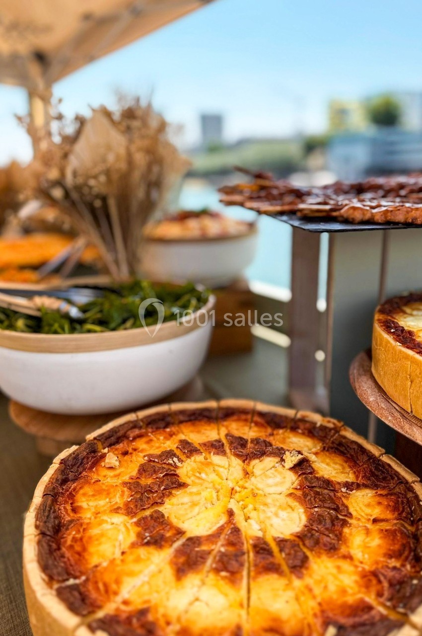 Quiches dorées, salade verte et brochettes grillées disposées sur une table en extérieur sous un parasol.