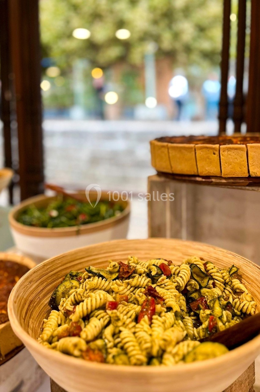 Salade de pâtes fusilli aux légumes dans un bol en bois, avec d'autres plats et un fond flou de jardin.