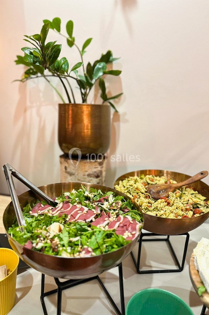 Deux saladiers en métal contenant une salade verte et une salade de pâtes, posés sur des supports devant une plante.