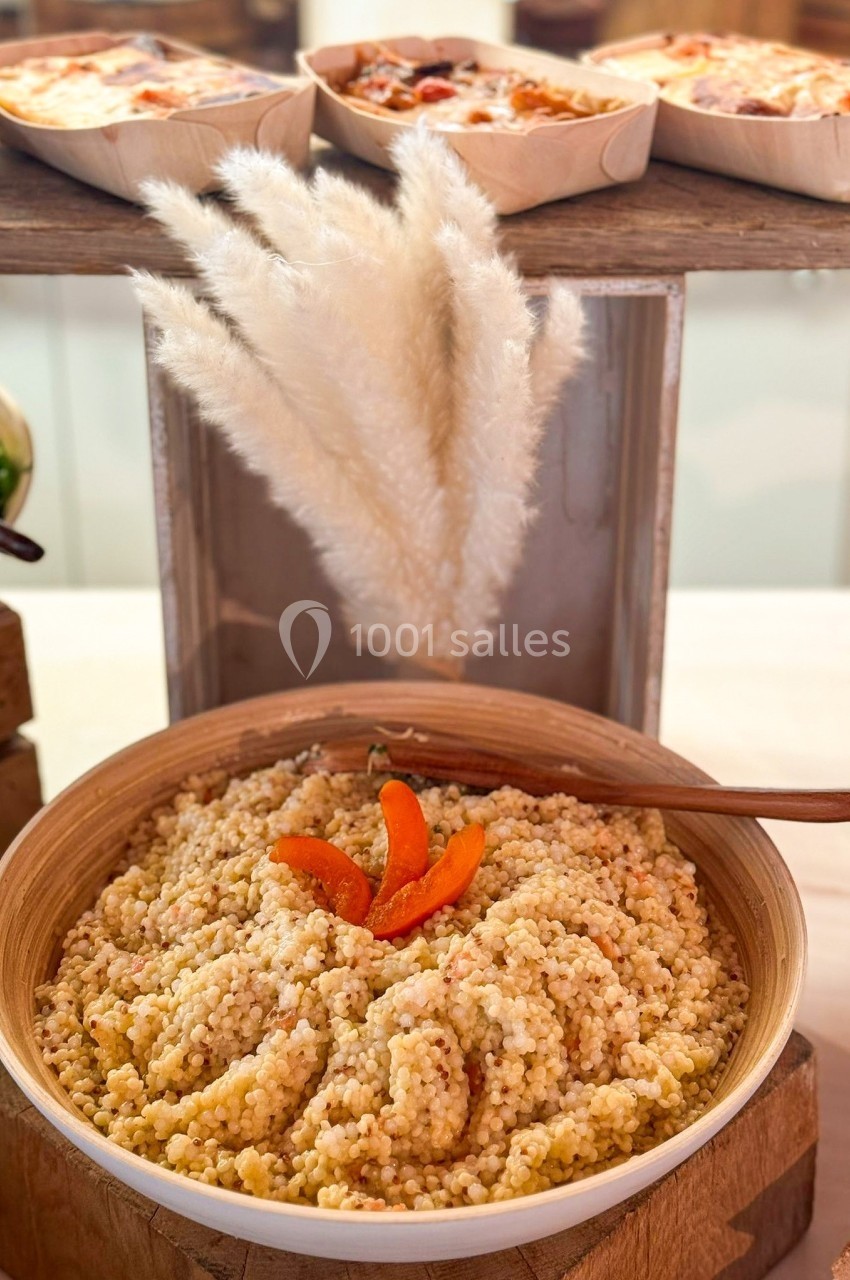 Bol de couscous perlé garni de morceaux d'abricots secs, présenté sur une table avec des plats en arrière-plan.