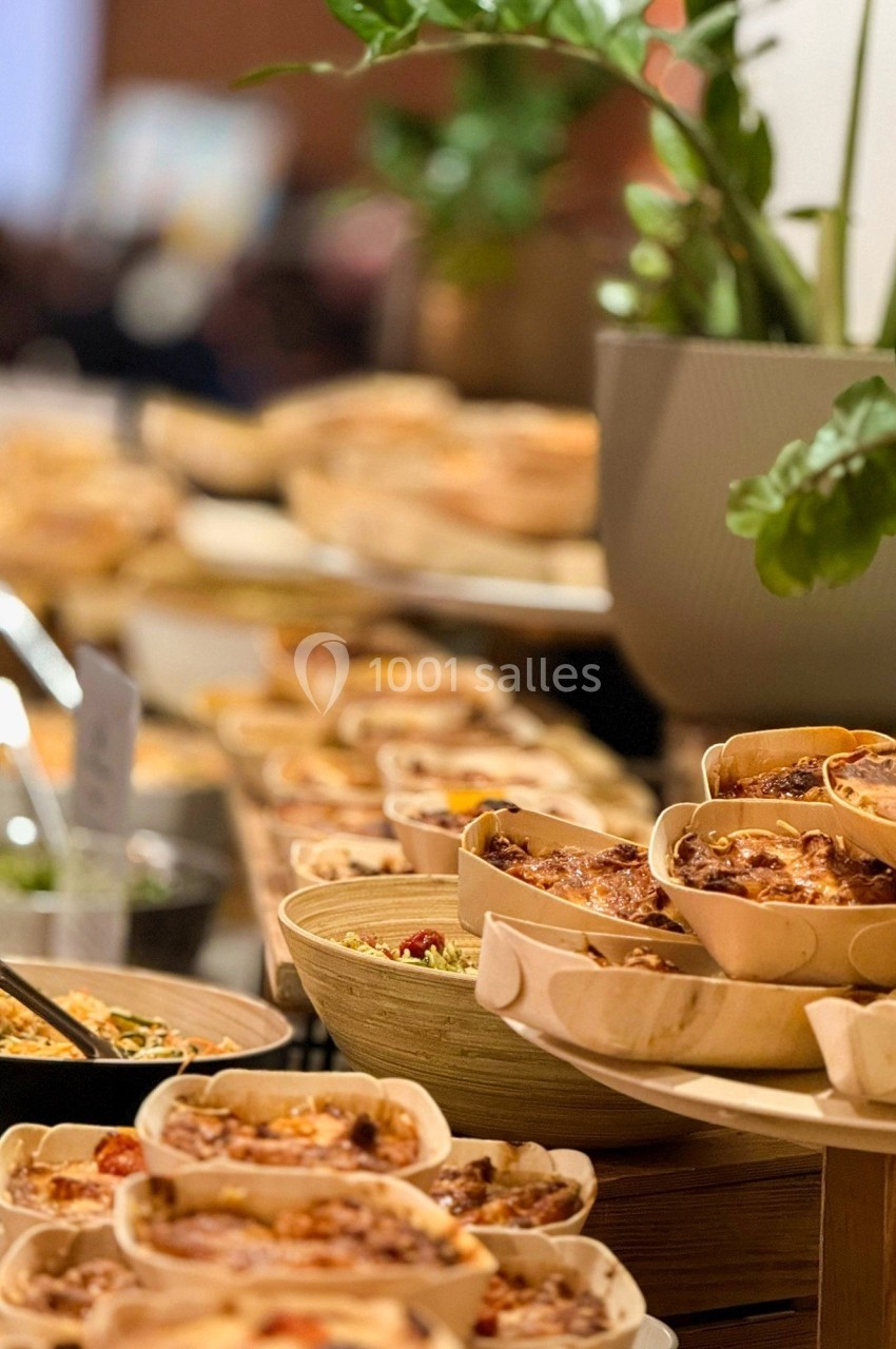 Buffet avec divers plats présentés dans des contenants individuels en bois, entouré de plantes décoratives.