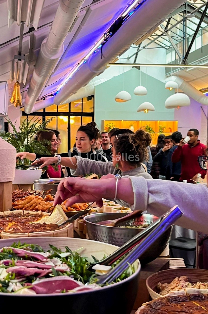 Buffet varié avec des plats salés et des convives se servant dans un espace lumineux et moderne.