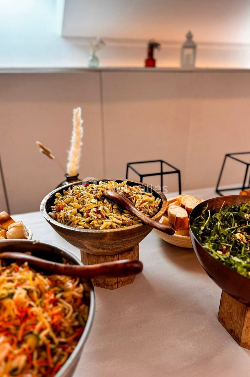 Buffet avec salades variées dans des bols en bois et métal, accompagné de pain sur une table blanche.