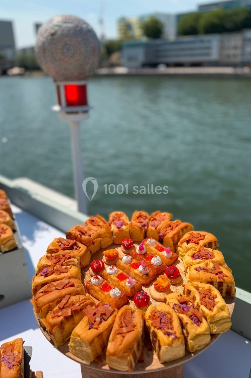 Plateau de pâtisseries variées disposées en cercle sur une table en extérieur, près d'un plan d'eau.