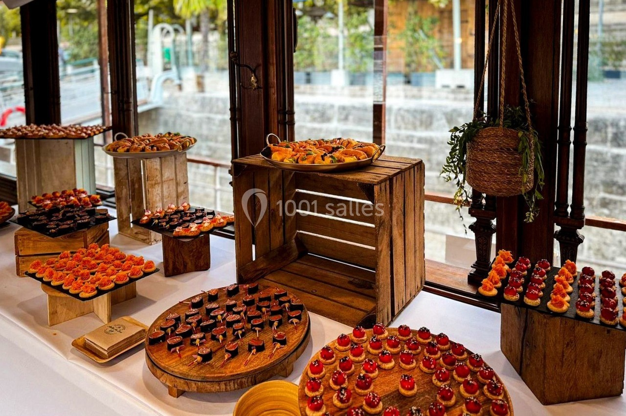 Buffet de canapés variés disposés sur des plateaux en bois, avec vue sur des fenêtres donnant sur l'extérieur.
