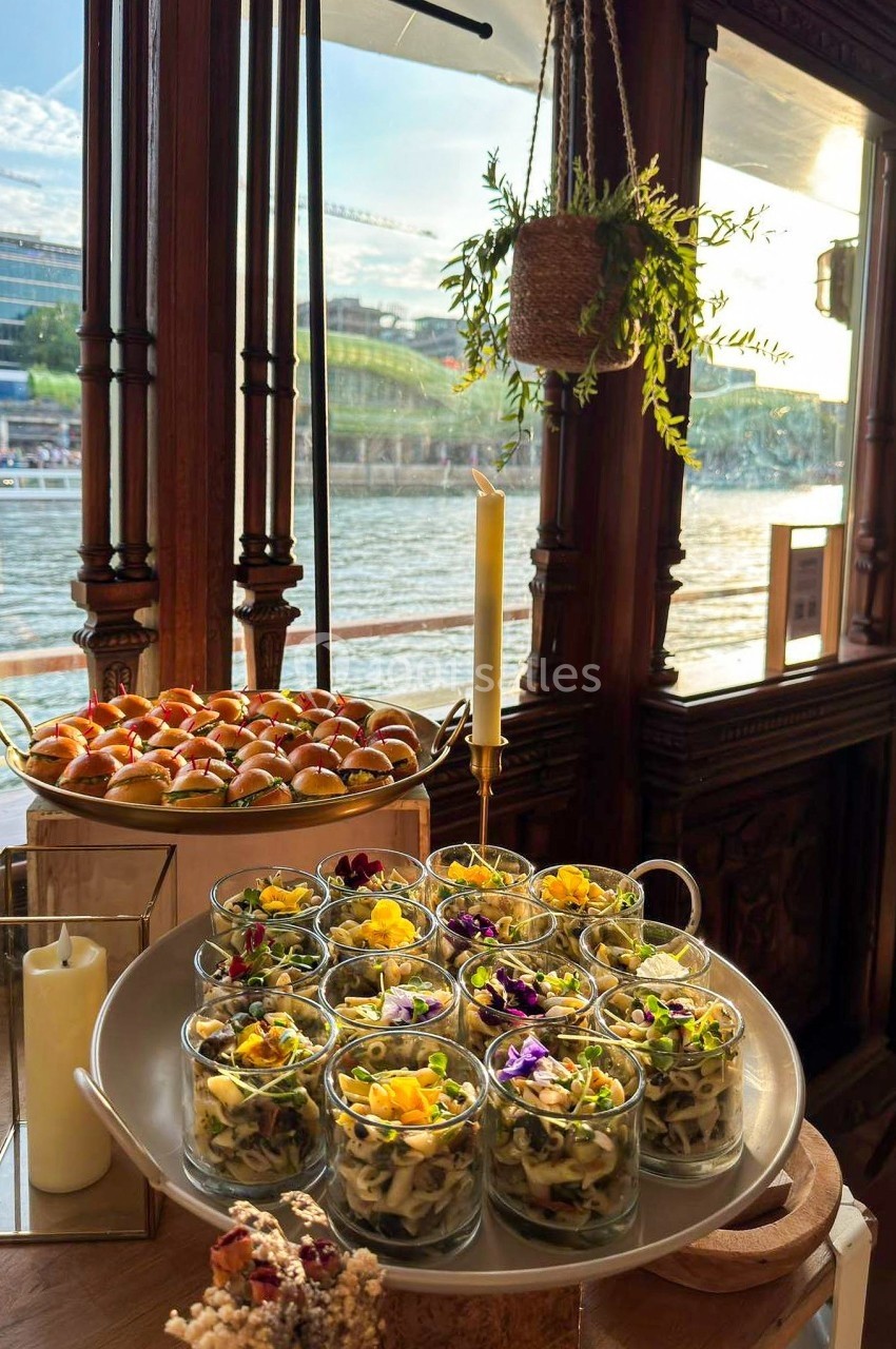 Plateau de verrines garnies de pâtes et fleurs comestibles, accompagné d'amuse-bouches, près d'une fenêtre donnant sur une…