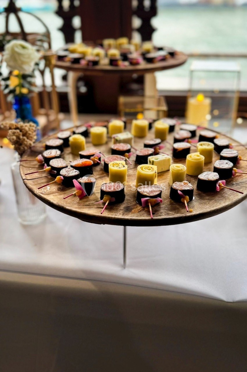 Plateau en bois garni de desserts variés, dont des bouchées au chocolat et des roulés jaunes, présenté sur une table blanche.