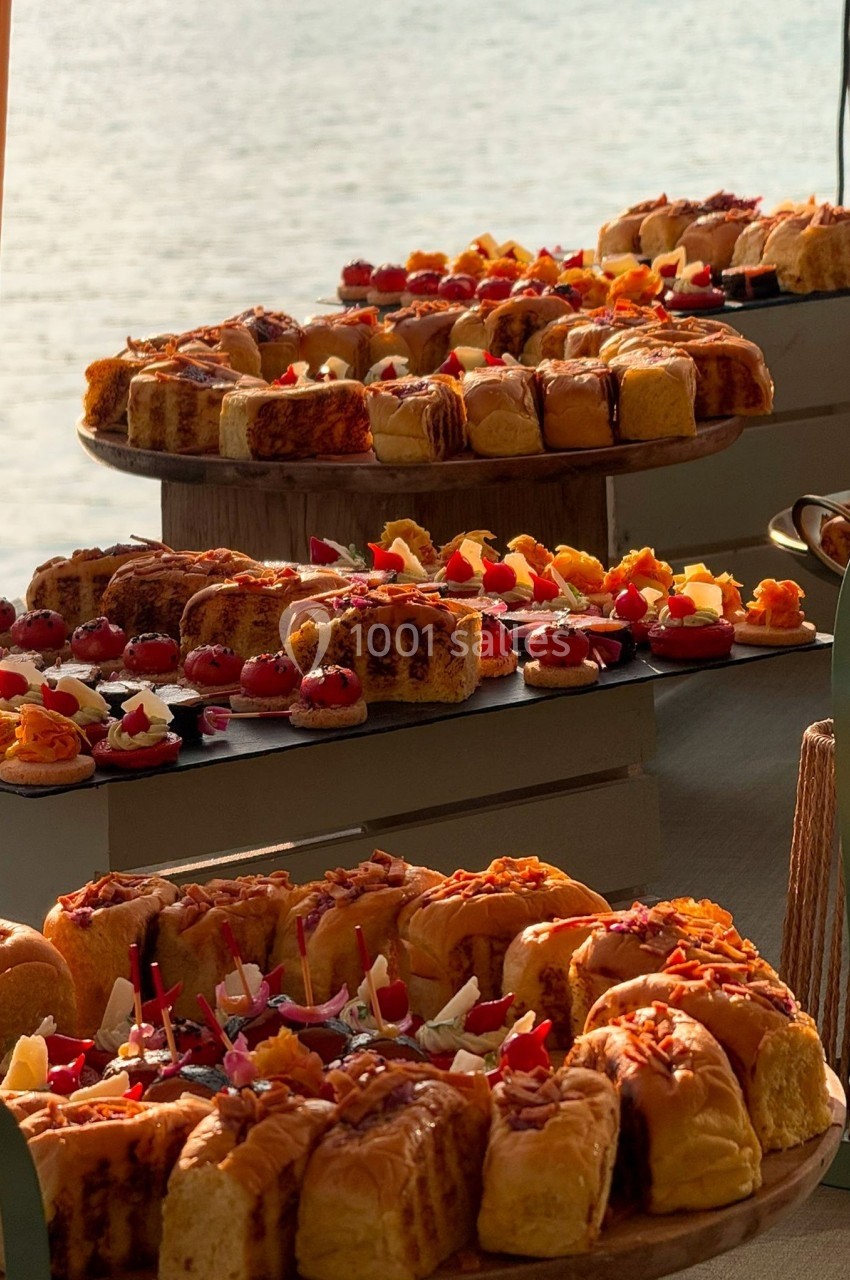 Plateaux de viennoiseries et pâtisseries variées disposés sur une table avec vue sur l'eau en arrière-plan.