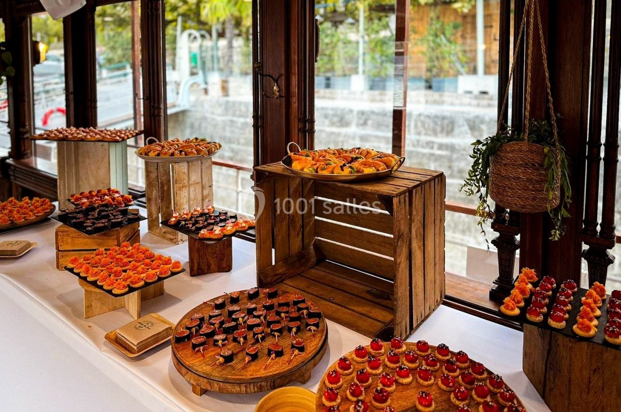 Buffet de petits fours variés disposés sur des présentoirs en bois près de grandes fenêtres donnant sur l'extérieur.