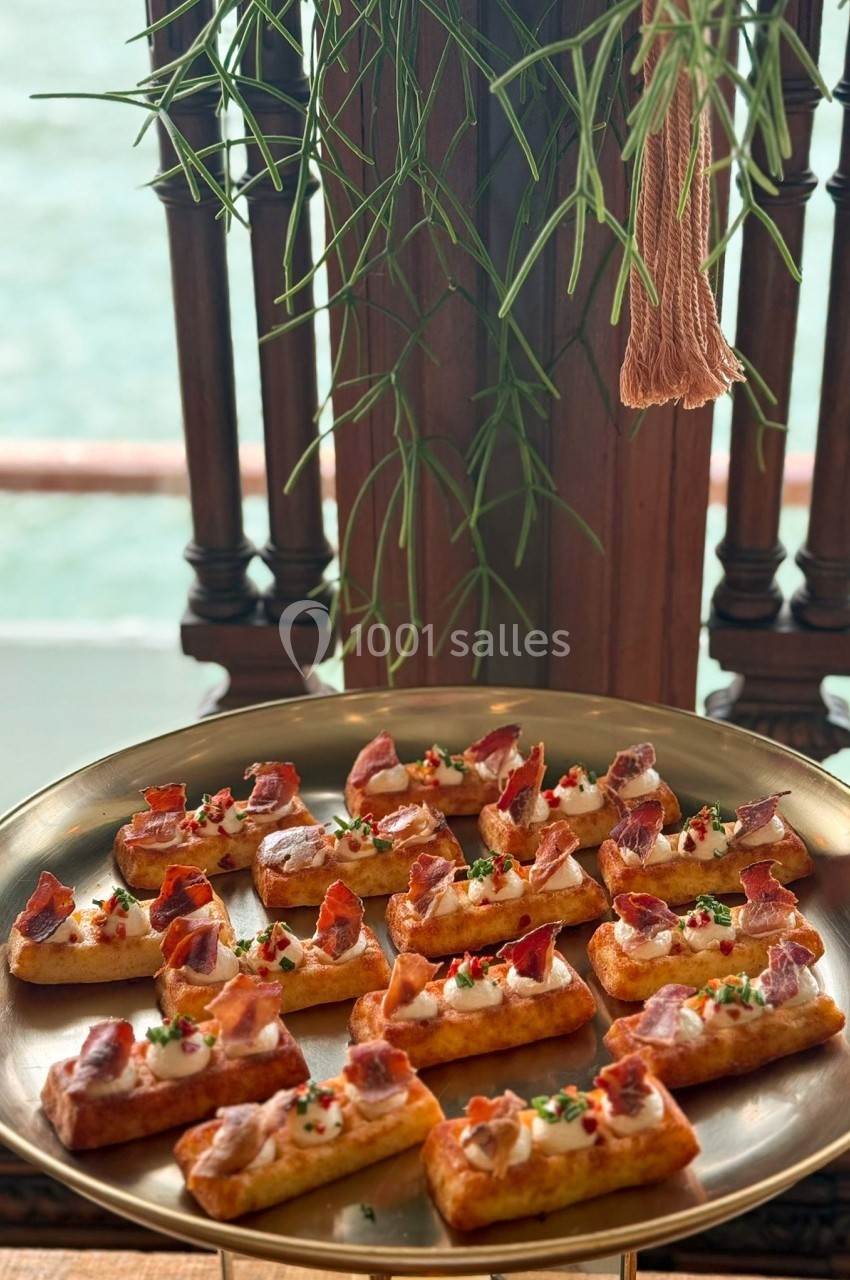 Plateau de bouchées apéritives garnies de crème, jambon et herbes, présenté sur une table près d'une fenêtre.