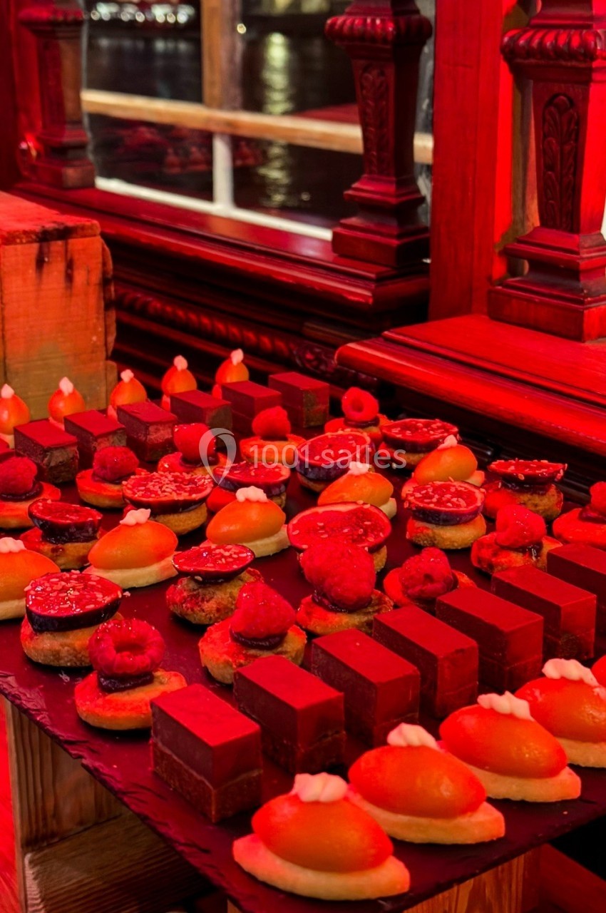 Plateau de desserts variés comprenant des pâtisseries et des chocolats, présenté sur une table dans un décor rouge…