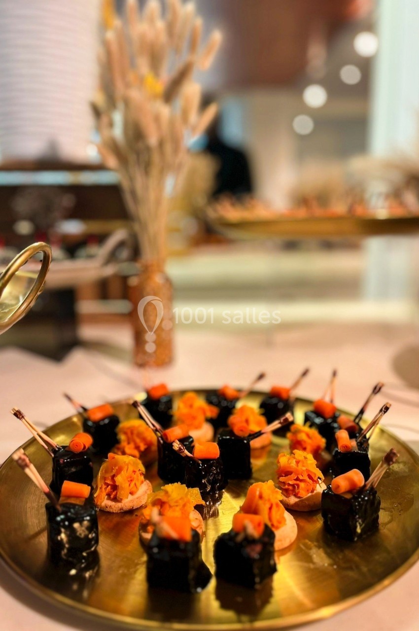 Plateau doré avec des amuse-bouches variés, incluant des bouchées noires et des toasts garnis de légumes colorés.