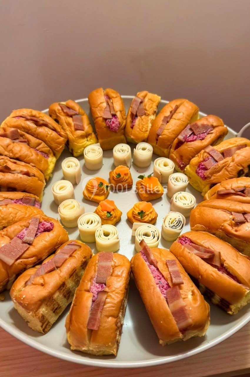 Assortiment de petits pains garnis de mousse rose et de morceaux de jambon, entourant des décorations en chocolat blanc.