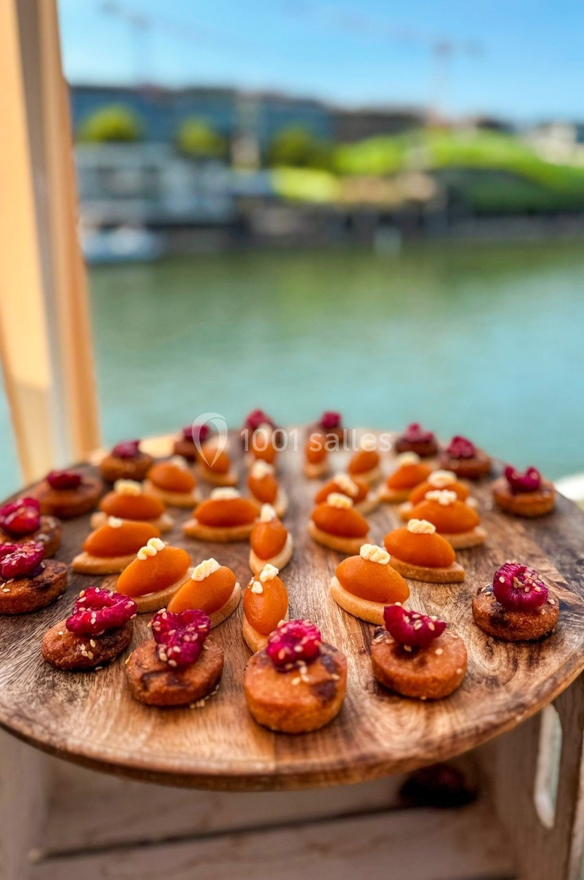 Plateau en bois garni de mignardises sucrées, disposé en extérieur près d'un plan d'eau sous un ciel dégagé.