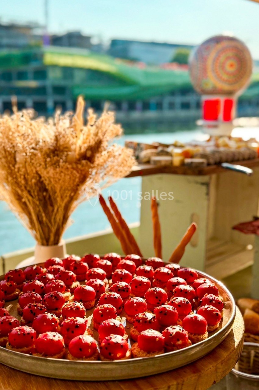 Plateau de petits choux rouges garnis, décoré de graines, posé sur une table en extérieur avec vue sur un fleuve.