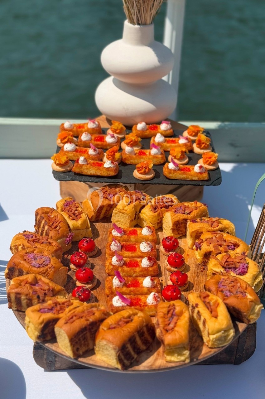 Plateau de mini-sandwichs et amuse-bouches variés disposés sur une table en extérieur près de l'eau.