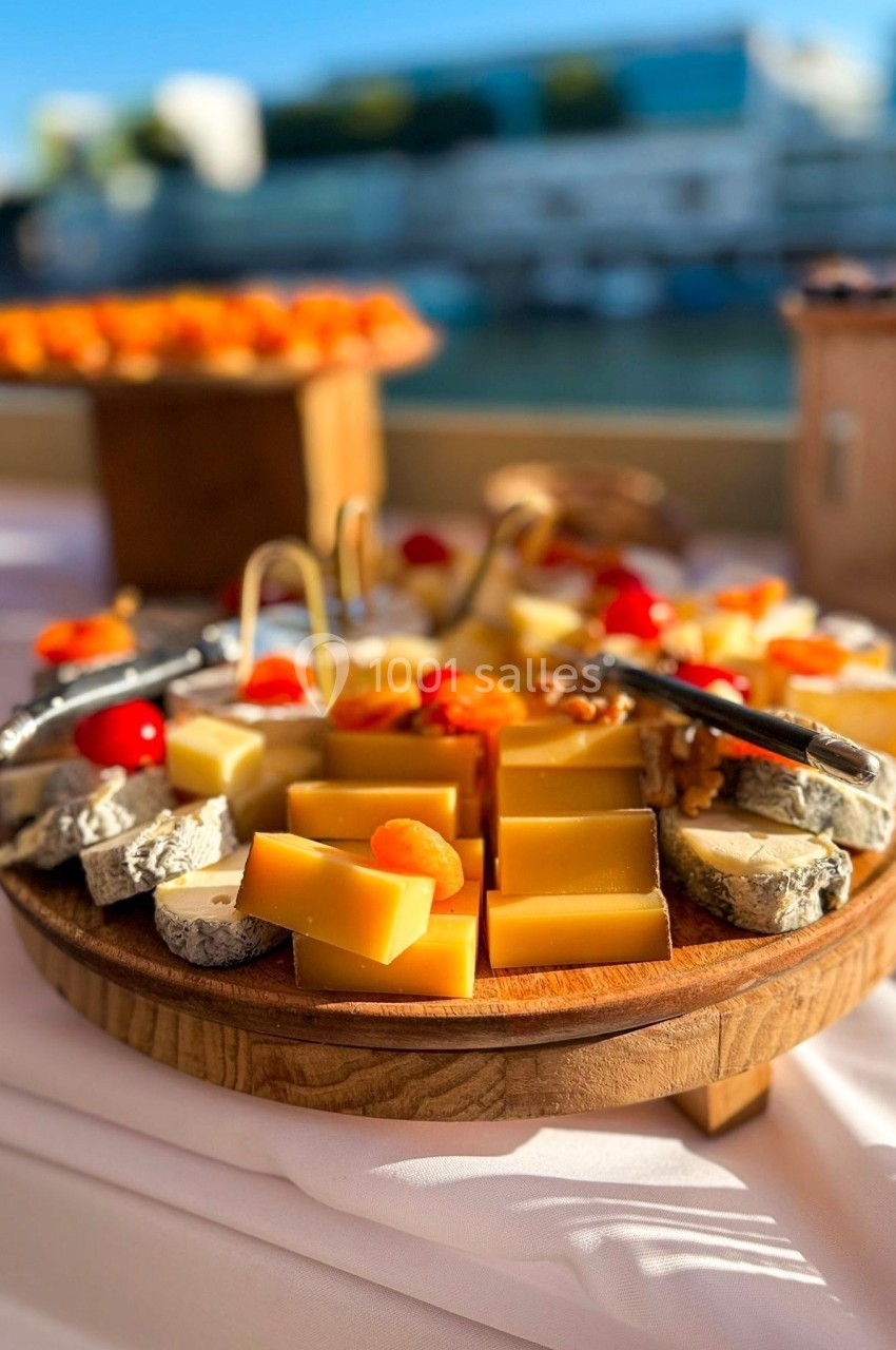 Plateau en bois garni de fromages variés, fruits secs et tomates cerises, présenté sur une table en extérieur.