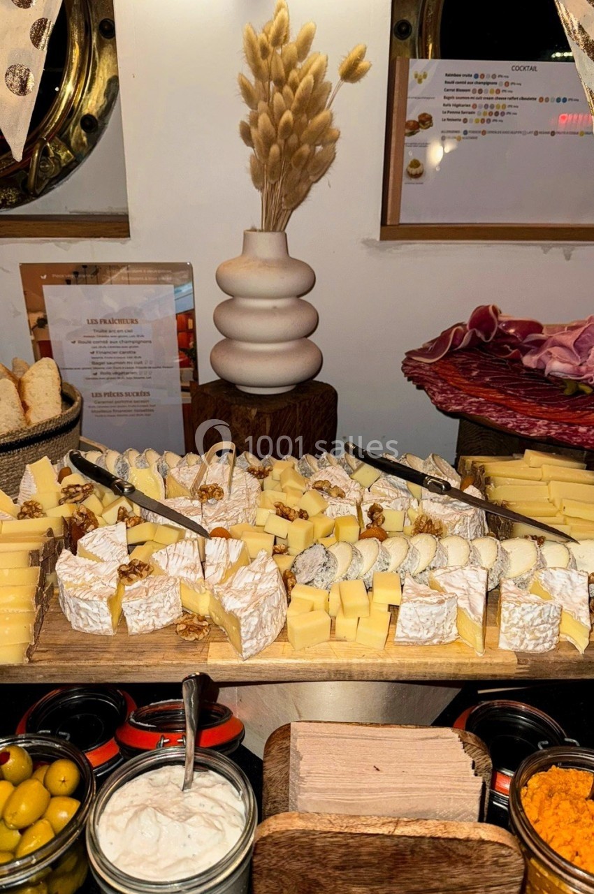 Plateau de fromages variés avec couteaux de service, accompagné de pain, olives et charcuterie sur une table décorée.
