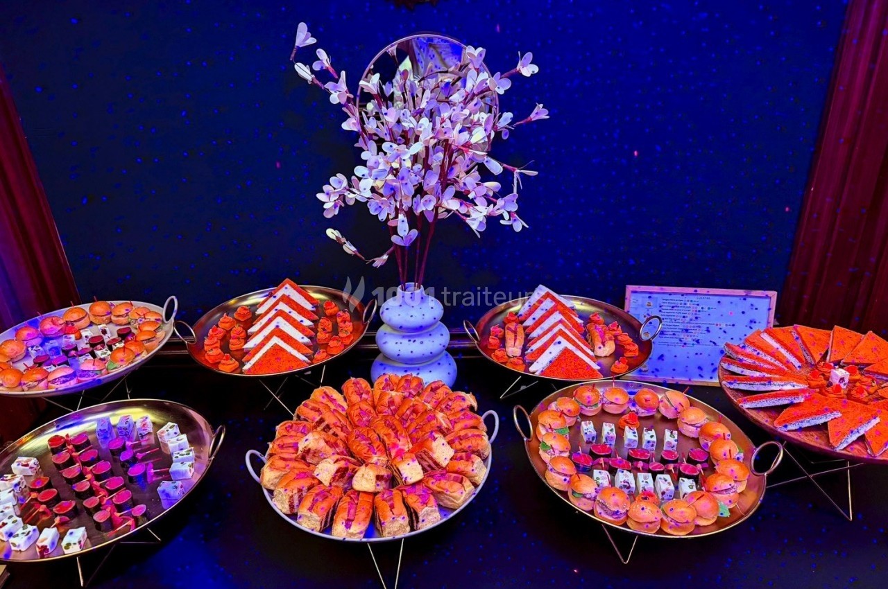 Plateau de desserts variés disposés sur des présentoirs, avec une décoration florale centrale et un éclairage coloré.