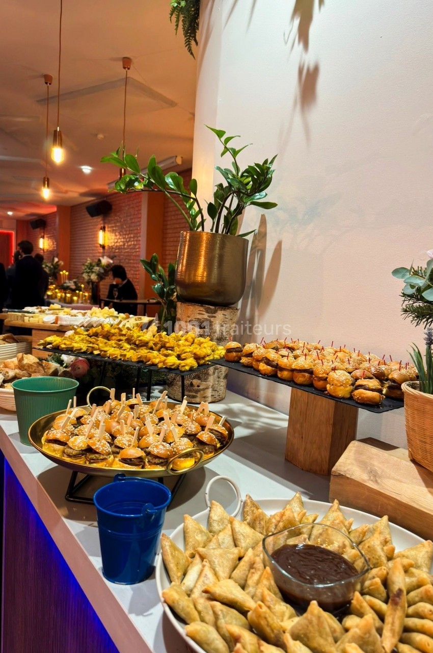 Buffet de réception avec assortiment de bouchées salées, samoussas, mini-burgers et sauces, dans un cadre lumineux et…