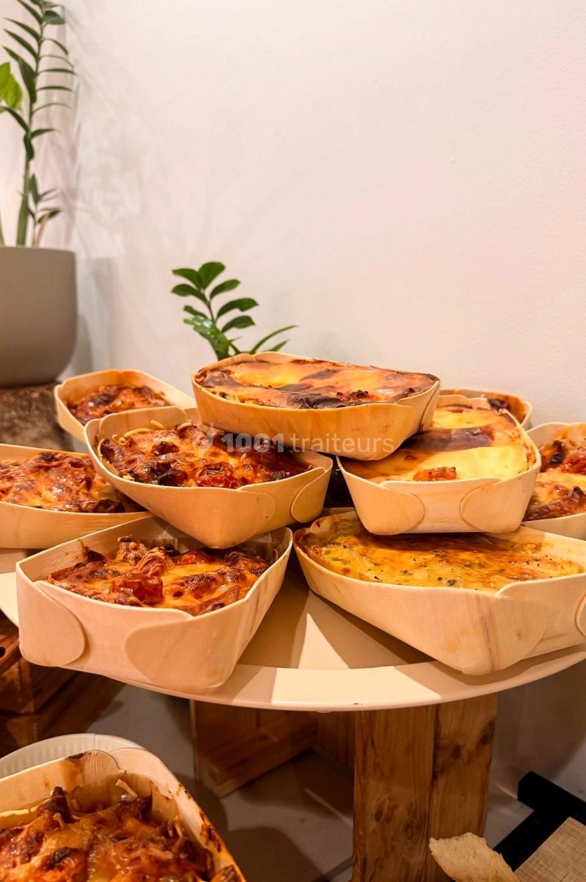 Quiches variées présentées dans des moules en bois, disposées sur une table en intérieur avec des plantes en arrière-plan.