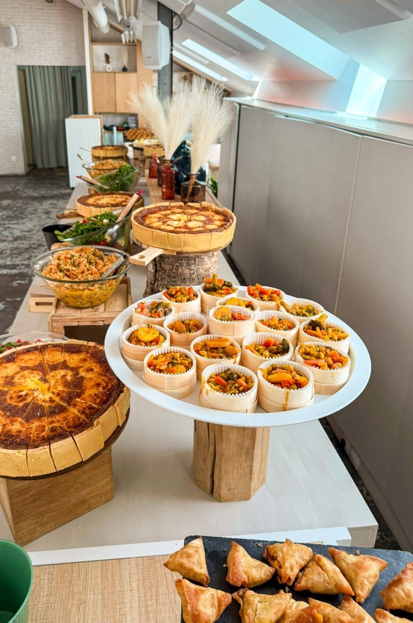 Buffet composé de quiches, samoussas, salades et verrines colorées, disposé sur une table dans un espace lumineux.