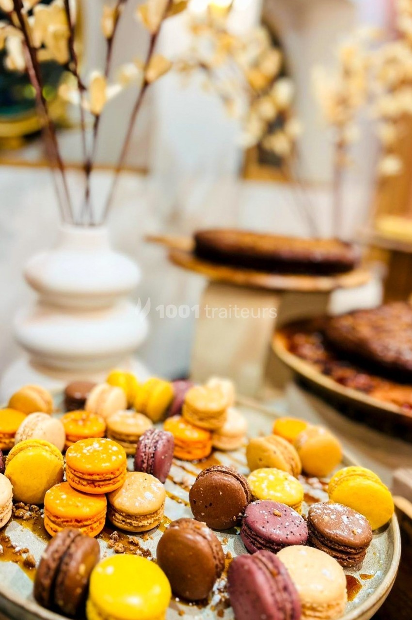 Assortiment de macarons colorés disposés sur un plateau, avec des desserts et une décoration florale en arrière-plan.