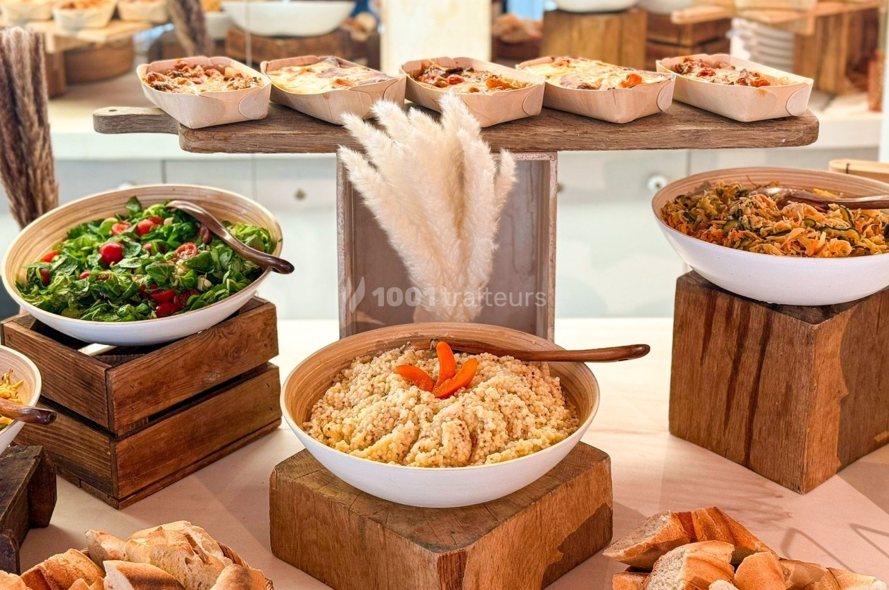 Buffet avec salades variées, pain, taboulé et plats cuisinés présentés sur des supports en bois.