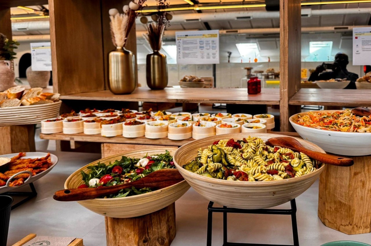 Buffet avec salades variées, verrines et pains disposés sur des présentoirs en bois dans un espace lumineux.