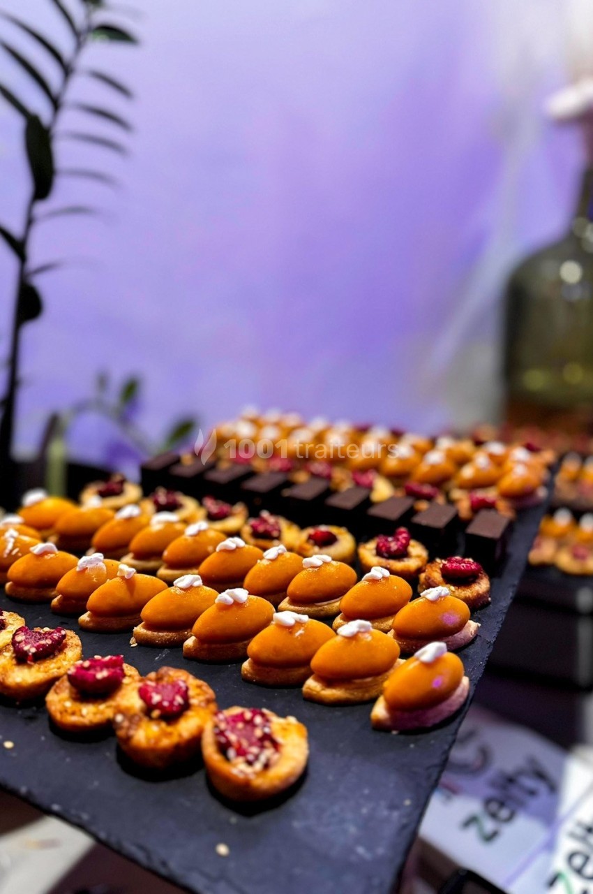 Plateau de mignardises variées, dont des tartelettes aux fruits rouges et des bouchées sucrées, présenté sur ardoise.
