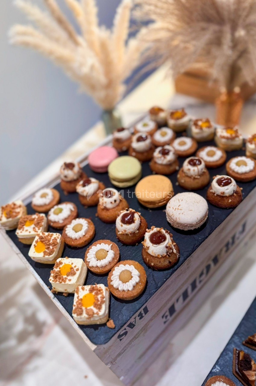 Plateau de pâtisseries miniatures variées disposées sur une caisse en bois, décoré avec des éléments végétaux secs.